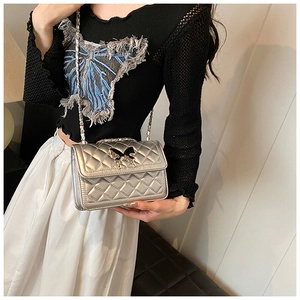 Détail du sac bandoulière matelassé argenté avec boucle papillon et bandoulière en chaîne
