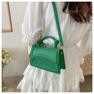 Detail of green leather handbag with wavy flap design and knotted handle on white dress