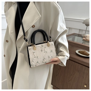 Detail of a straw tote bag with floral embroidery and black woven handles on trench coat