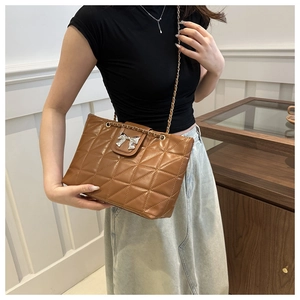 Quilted caramel chain shoulder bag with silver bow detail shown on a model outfit