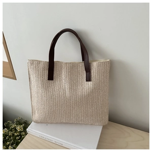 Detail of woven straw tote bag with brown leather handles and natural texture on a desk