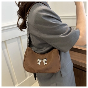 Close-up of brown crescent bag featuring a silver metal bow and chain strap detail