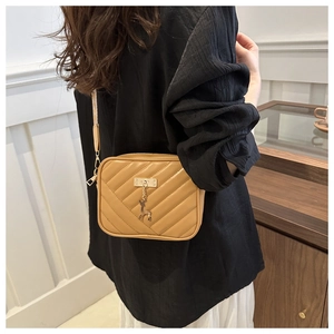 Detail of yellow quilted crossbody bag with golden deer pendant worn by a model