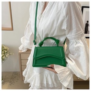 Detail of green leather handbag with knot handle and adjustable strap worn with white dress