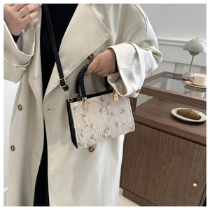 Detail of floral embroidery on a cream straw tote bag with black handles and shoulder strap
