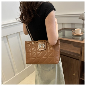 Detail of a brown quilted tote bag with a silver bow and metal chain strap
