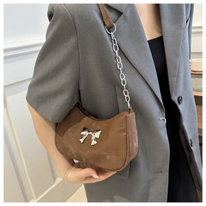 Detail of a brown crescent-shaped underarm bag with silver bow hardware and chain strap