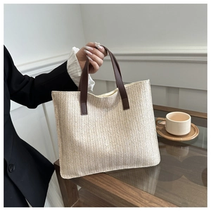 Close-up of beige woven tote bag with brown handles and detailed herringbone texture