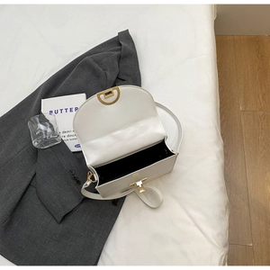 Detail of white crossbody bag showing golden buckle, black lining, and matte leather texture
