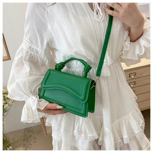 Detail of bright green crossbody bag with knot handle worn over a white lace dress