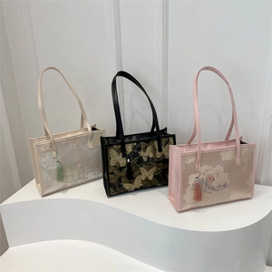 Trois sacs cabas brodés de motifs floraux et pompons sur un présentoir blanc