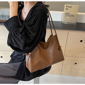 Detail of a large brown faux leather tote bag with knot accent worn on the shoulder