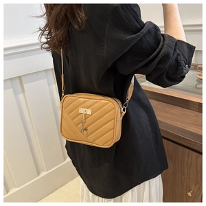 Chic light brown crossbody bag with gold deer charm shown on model in minimal room