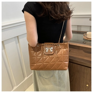 Close-up of brown quilted tote bag with silver bow buckle and elegant chain strap