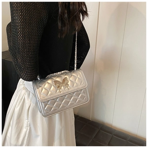Sac argenté matelassé avec fermoir papillon et chaîne porté par un mannequin