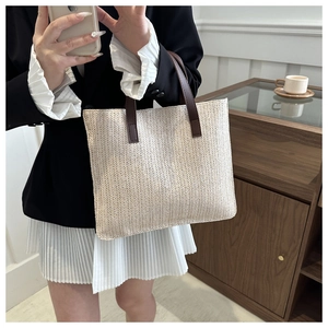 Detail view of beige woven tote bag with dark coffee leather handles on a female model