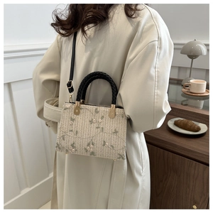 Detail view of woven cream crossbody bag featuring floral embroidery and cord handle