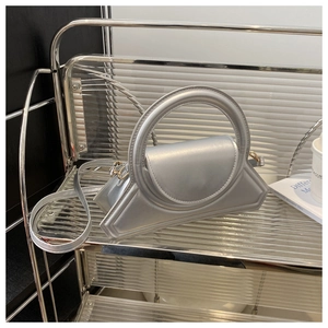 Dettaglio borsa geometrica argento con manico rotondo su scaffale in metallo