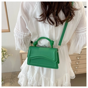 Detail of green crossbody bag with wavy embossing and knotted handle on white dress