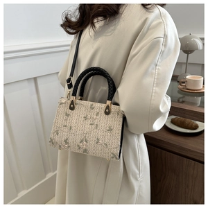 Detail of a beige woven handbag featuring green flower embroidery and a black leather handle