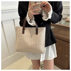 Close-up of beige woven texture and brown leather handles on a minimalist tote bag