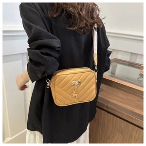 Chic mustard yellow crossbody bag with quilted texture and gold deer charm on a model