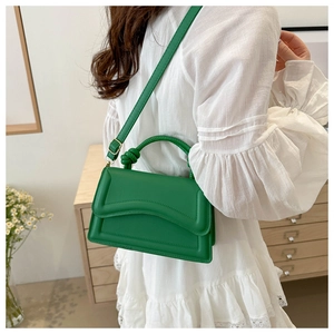 Close-up of vibrant green handbag with knot handle detail on a white lace dress