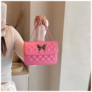 Détail d'un sac à bandoulière rose matelassé avec fermoir papillon argenté tenu par un mannequin