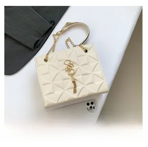 Detail of beige quilted square bag with gold chain strap and letter pendant on white surface