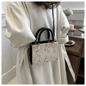 Detail of floral embroidery on a mini beige woven tote with black handles and strap