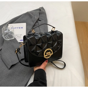 Detail of black quilted crossbody bag with golden rotary lock on a grey suit background