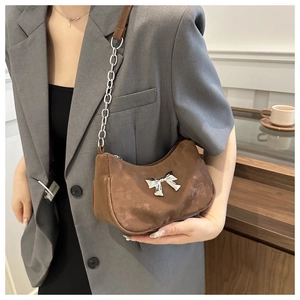 Brown crescent underarm bag with silver bow detail and metallic chain strap on model