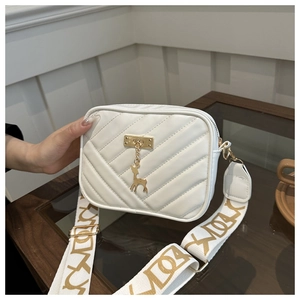 Detail of white quilted crossbody bag featuring gold deer charm and wide lettered strap
