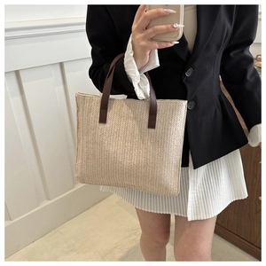 Detail of the woven tote bag featuring cream straw texture and dark brown leather handles