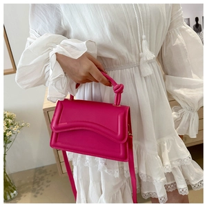 Detail of hot pink crossbody bag with wavy flap and decorative knot handle design