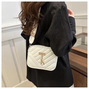Detail of white quilted crossbody bag with golden deer charm and wide shoulder strap