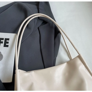 Close-up of cream leather shoulder bag with slim handle against a grey suit background