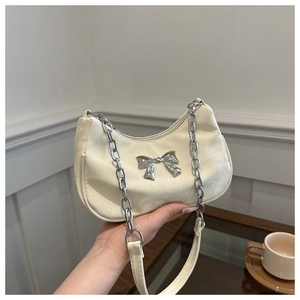 Detail of a creamy white leather handbag featuring a silver metallic bow and chunky chain