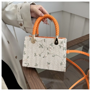 Close-up of woven straw bag with floral embroidery and orange woven handle detail