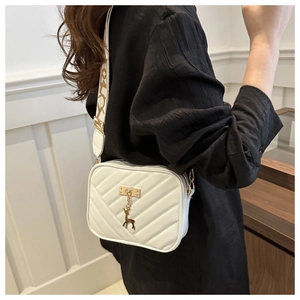 White quilted crossbody bag with golden deer charm and wide pattern strap shown on model