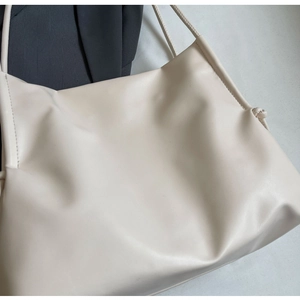 Detail of minimalist beige leather tote with slim shoulder strap and elegant side knot