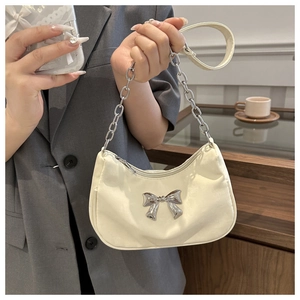 Detail of cream shoulder bag featuring a metallic silver bow and chunky chain strap