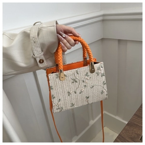 Detail of floral embroidery on beige woven straw handbag with orange leather handle
