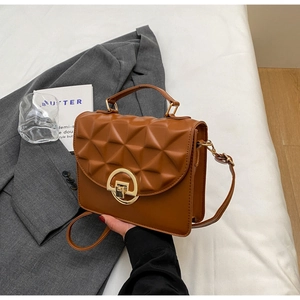 Detail of brown geometric 3D embossed texture and gold round twist lock on shoulder bag
