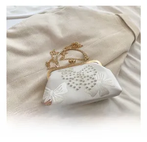Close-up of white satin evening bag featuring handcrafted pearl bow and gold chain strap