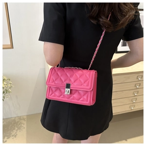 Detail of quilted bright pink crossbody bag with silver chain strap worn by a model