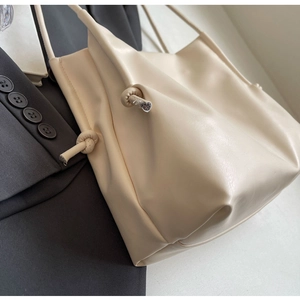 Close-up of beige tote bag with knot detail on dark grey suit background