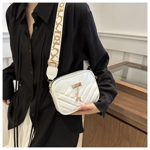 Detail of white quilted crossbody bag featuring V-shaped stitching and gold deer charm