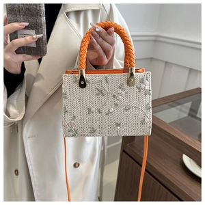 Close-up of beige woven straw handbag with intricate white floral embroidery and orange handle