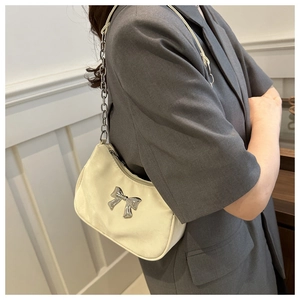 Chic cream-colored underarm bag with silver bow accent and metal chain strap on model